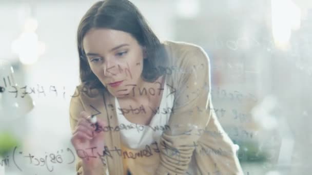 Nahaufnahme einer schönen und kreativen Frau, die Formeln auf ein gläsernes Whiteboard schreibt. — Stockvideo