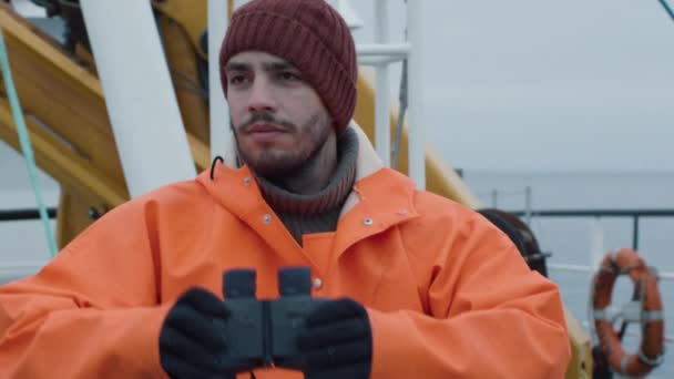 Capitán de barco de pesca comercial vestido con capa protectora Mirando a través de prismáticos — Vídeo de stock