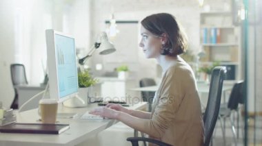 Kişisel bilgisayar kullanarak masasında oturan genç güzel kadın çalışıyor. O bir Modern Lightsome ofis mekanları çalışıyor.