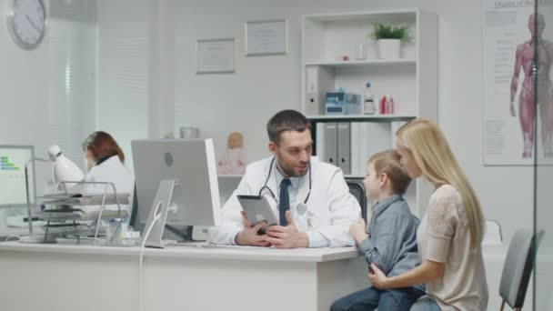 Mannelijke arts raadpleegt jonge jongen en zijn moeder met behulp van een Tablet. Ze glimlachen en Joke harte. — Stockvideo
