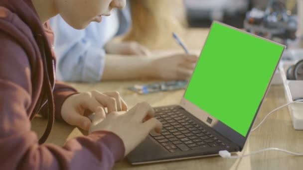 Rapaz inteligente trabalha em um laptop com tela verde falsa em sua classe de ciência da computação . — Vídeo de Stock