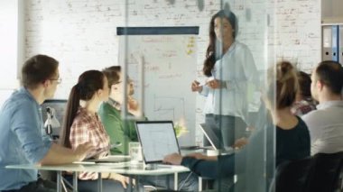 Kadın onun yaratıcı ofis personeli için beyaz tahta sunum yapıyor. Büyük cam masa notlar alarak açık dizüstü bilgisayarlar ile iş arkadaşlarınızla oturup. Office şık ve parlak olduğunu.