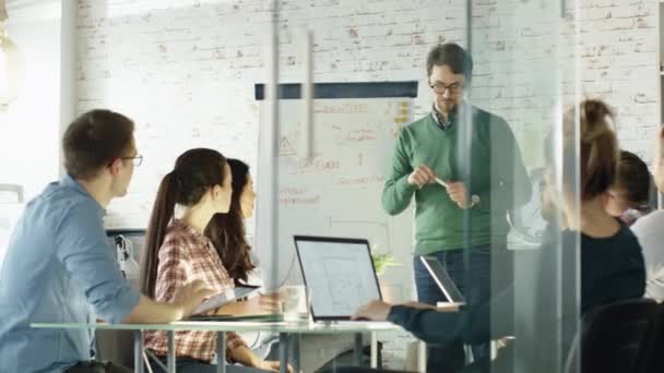 Energisk Man gör Whiteboard Presentation till sin kreativa kontorspersonal. Medarbetare sitta vid bordet stora glas med öppen bärbara datorer, anteckningar. Office är snygg och Bright. — Stockvideo