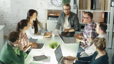 Yaratıcı gençlerin grup stratejik planlama oturum var. Onlar kendi parlak ve Modern Loft Office Açık dizüstü bilgisayarlar ile büyük cam masada oturuyorlar.