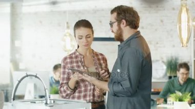 Güzel yaratıcı kız ve onun şık erkek meslektaşı tartışmak iş ile ilgili konularda Tablet bilgisayar. Arka planda çalışan genç insanlar ile yaratıcı Office içinde bulundukları.
