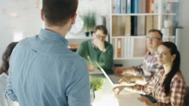 Jonge uitvoerende adressen zijn collega's op een sessie van strategische Planning. Hij staat en collega's zitten op het grote conferentie tabel luisteren naar hem zorgvuldig. Slow Motion. — Stockvideo