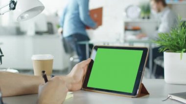Yakın çekim yeşil ekran Tablet bilgisayar tutarak ve notlar üzerinde yapışkan kağıt yapma bir adamın elleri. Arka plan parlak Modern ofiste insanlar bu çalışma ile.