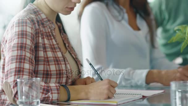 Frau macht sich Notizen, während sie am Konferenztisch inmitten hitziger Diskussionen sitzt. — Stockvideo