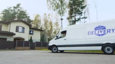 Kargo minibüs banliyö evine ve teslimat adam ortaya çıkıyor. Arka plan üzerinde sarı ağaç ve çam ağaçları ile güneşli Sonbahar geldi.