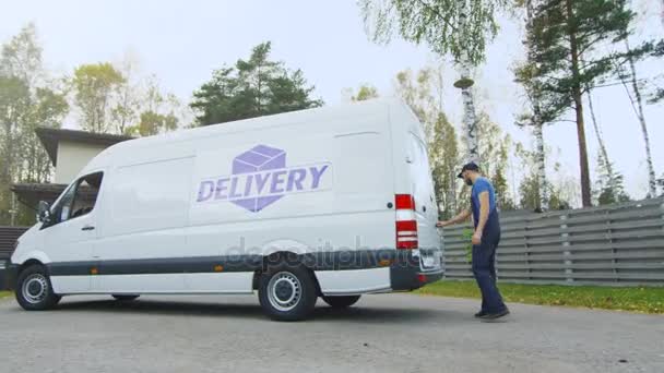 Delivery Man saca cajas de cartón de su furgoneta de carga. En un área suburbana. Otoño soleado con abedules y pinos amarillos está en el fondo . — Vídeos de Stock