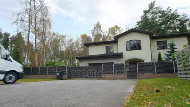 Gran furgoneta blanca conduce a la hermosa casa suburbana. El hombre sale de la camioneta. Afuera es claramente visible la temporada de otoño . — Vídeos de Stock