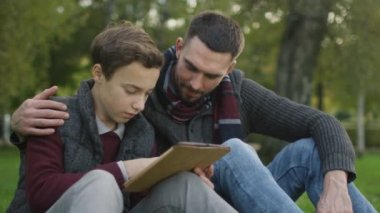 Oğul ve baba parkta oturan Tablet kullanma