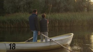 Baba ve oğul teknede Balık tutma sırasında ayakta duruyorlar. Oğlum salıncaklar olta. 