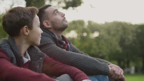 Padre e Hijo están sentados en el parque y hablando. Padre abrazos hijo . — Vídeos de Stock