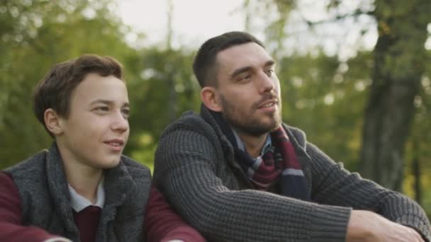 Vater und Sohn sitzen im Park und unterhalten sich. Sohn umarmt Vater. — Stockvideo