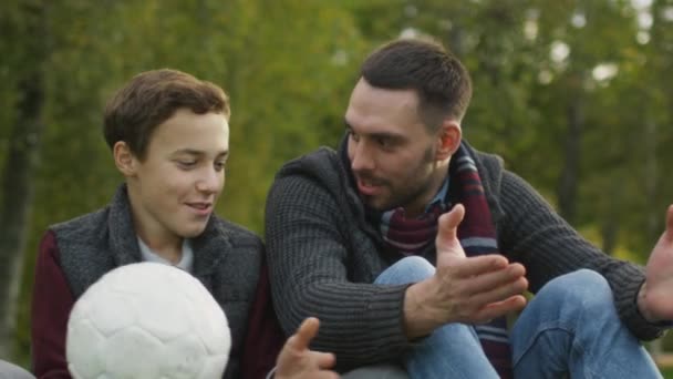 Πατέρας και γιος μιλούν στο πάρκο. Γιος κρατά μπάλα. — Αρχείο Βίντεο