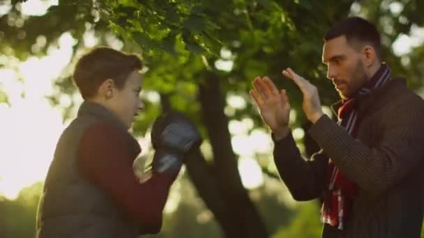 Zoon en vader boksen in het Park. Zoon in bokshandschoenen Hits vaders handen. — Stockvideo