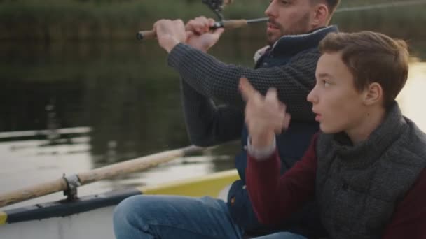 Vater bringt seinem Sohn das Angeln bei. Beide sitzen im Boot. — Stockvideo