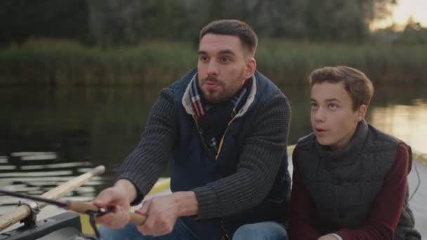 Vater und Sohn sitzen im Boot beim Angeln. Vater schwingt Angelrute. — Stockvideo