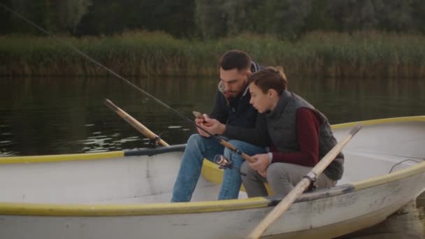 Pai e filho estão usando Smartphone enquanto a pesca do barco — Vídeo de Stock