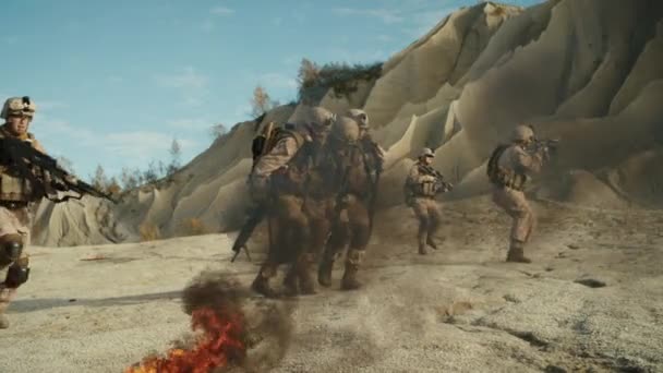 Soldaten, die einen Verletzten tragen, während andere Mitglieder der Truppe sie während einer Militäroperation in der Wüste decken. Zeitlupe. — Stockvideo