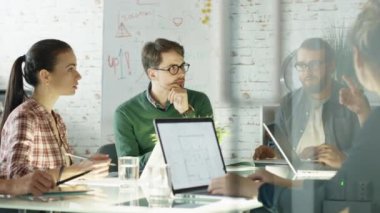 Yaratıcı gençlerin grup stratejik planlama oturum var. Onlar kendi parlak ve Modern Loft Office Açık dizüstü bilgisayarlar ile büyük cam masada oturuyorlar.