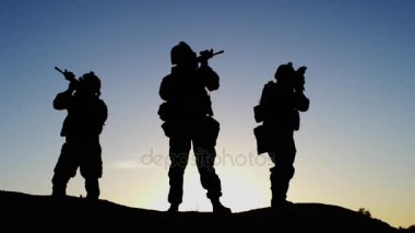 Çöl ortamında'nde Günbatımı ışık duran üç tam donanımlı ve silahlı asker kadrosu. Ağır çekim.
