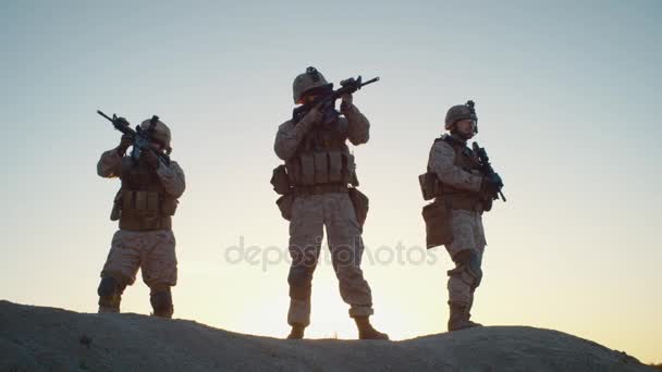 Escuadrón de tres soldados totalmente equipados y armados de pie en la colina en el entorno del desierto bajo la luz del atardecer. Moción lenta . — Vídeos de Stock
