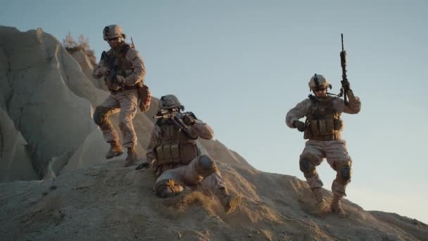 Grupp fullt utrustade och beväpnade soldater flyttar ner för backen i öknen. — Stockvideo