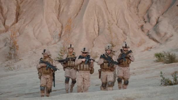 Grup tam donanımlı ve silahlı asker ileri çöl ortamında kameraya doğru yürüyüş. — Stok video