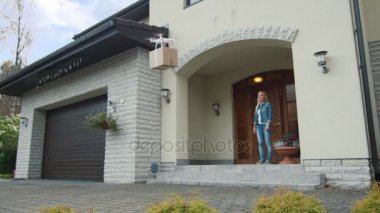 Uçak uçan onun posta paketi ona sunarken gülümseyen kadın bir verandada duruyor.