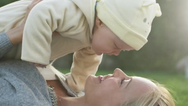 Mère embrasse son bébé tout en s'allongeant sur l'herbe . — Video