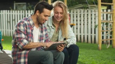 Genç adam ve kadın dokunmatik Tablet bilgisayar biraraya istimal, onlar are arka bahçesinde üzerinde parlak yaz gününde.