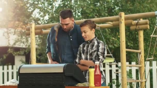 Le père et le fils cuisinent des hamburgers sur le gril à la journée d'été lumineuse . — Video