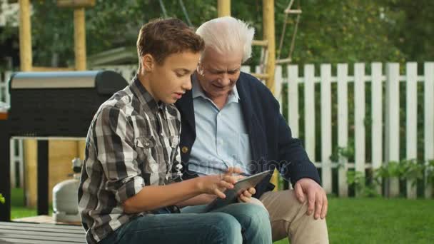 Młody chłopak pokazuje się starszy człowiek jak używać komputera typu Tablet z ekranem dotykowym. — Wideo stockowe