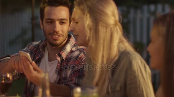 Красавчик, использующий мобильный телефон и показывающий содержимое своей подружке во время семейного ужина . — стоковое видео