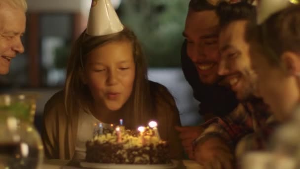 Feliz chica sonriente soplando velas en su pastel de cumpleaños. Chica rodeada por su familia y amigos — Vídeos de Stock