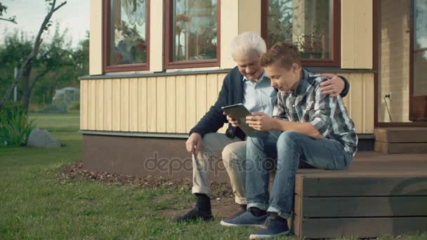 Внук учит дедушку пользоваться планшетным компьютером — стоковое видео