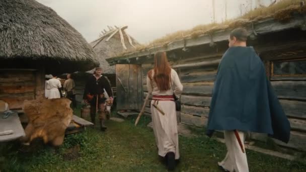 Люди, одетые в средневековую одежду, играют жизнь скандинавских граждан в деревне во время фестиваля славян и викингов . — стоковое видео