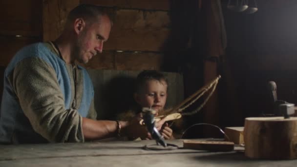 Gekleed in middeleeuwse kleding Man spelen met zoon, leert hem, rol spelen leven van Scandinavische civiele mensen in het dorp tijdens de slaven en Vikingen Festival. — Stockvideo