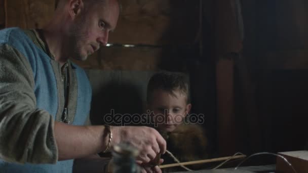 Vestido con ropa medieval Hombre Jugando con el Hijo, enseñándole. Juego de rol La vida de los ciudadanos escandinavos en la aldea durante el Festival de Eslavos y Vikingos . — Vídeo de stock