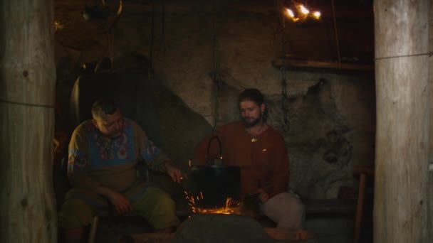 In mittelalterlichen Gewändern gekleidete Menschen entspannen sich, reden, trinken und kochen, das Leben der Zivilbevölkerung im Dorf. Mittelalterliche Reenactment. — Stockvideo