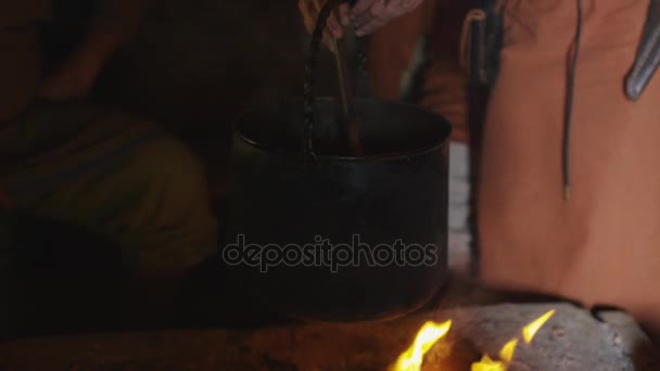 Gekleed in middeleeuwse kleding vrouw koken van een maaltijd in brand. Middeleeuwse re-enactment. — Stockvideo