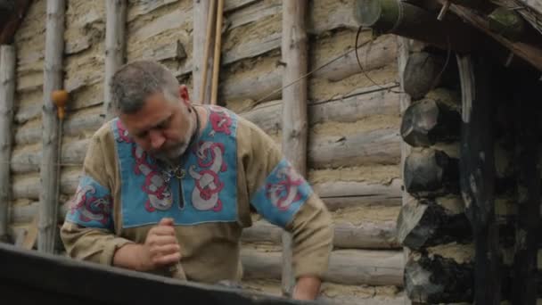 Life of Civilian People at the Village. Dressed in Medieval Clothing Man Makes a Boat. Medieval Reenactment. — Stock Video