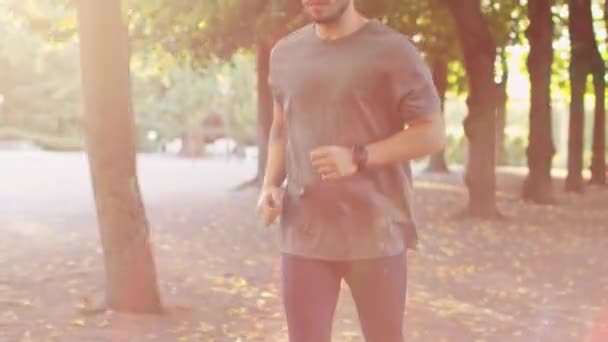 Όμορφος νεαρός, χρησιμοποιώντας έξυπνο ρολόι κατά τη διάρκεια πρωί τρέχει στο πάρκο — Αρχείο Βίντεο