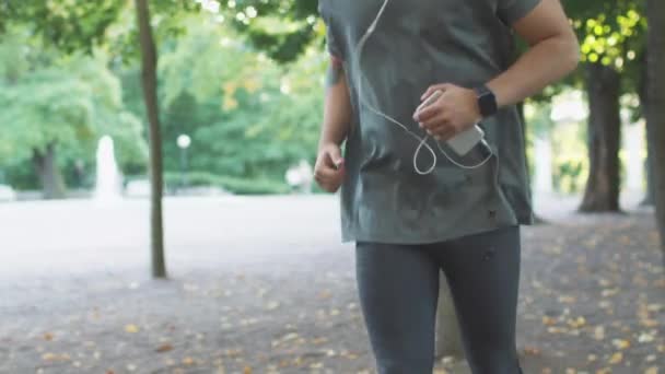 Ο άνθρωπος χρησιμοποιεί κινητό τηλέφωνο ενώ τρέχει στο πάρκο στο λαμπρό ηλιόλουστη μέρα — Αρχείο Βίντεο