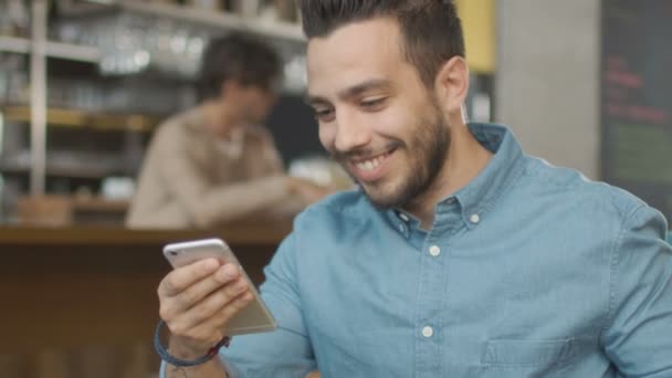 Hiszpanie etniczna młody człowiek przy użyciu telefonu komórkowego w przytulnej kawiarni. — Wideo stockowe