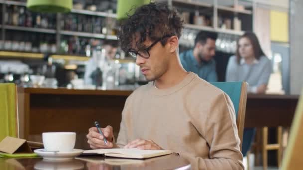 Joven de etnia hispana usando Tablet Computer y tomando notas en un cuaderno en la acogedora cafetería . — Vídeo de stock