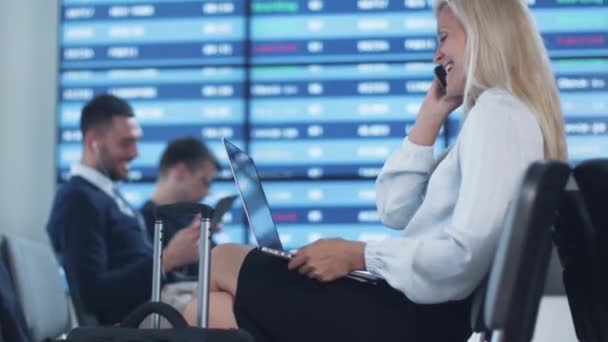 Atractiva mujer de negocios adulta hablando por teléfono mientras espera el embarque en la sala de embarque en el aeropuerto . — Vídeo de stock