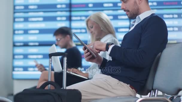 Hombre usando Tablet mientras espera el embarque en la sala de embarque en el aeropuerto . — Vídeos de Stock